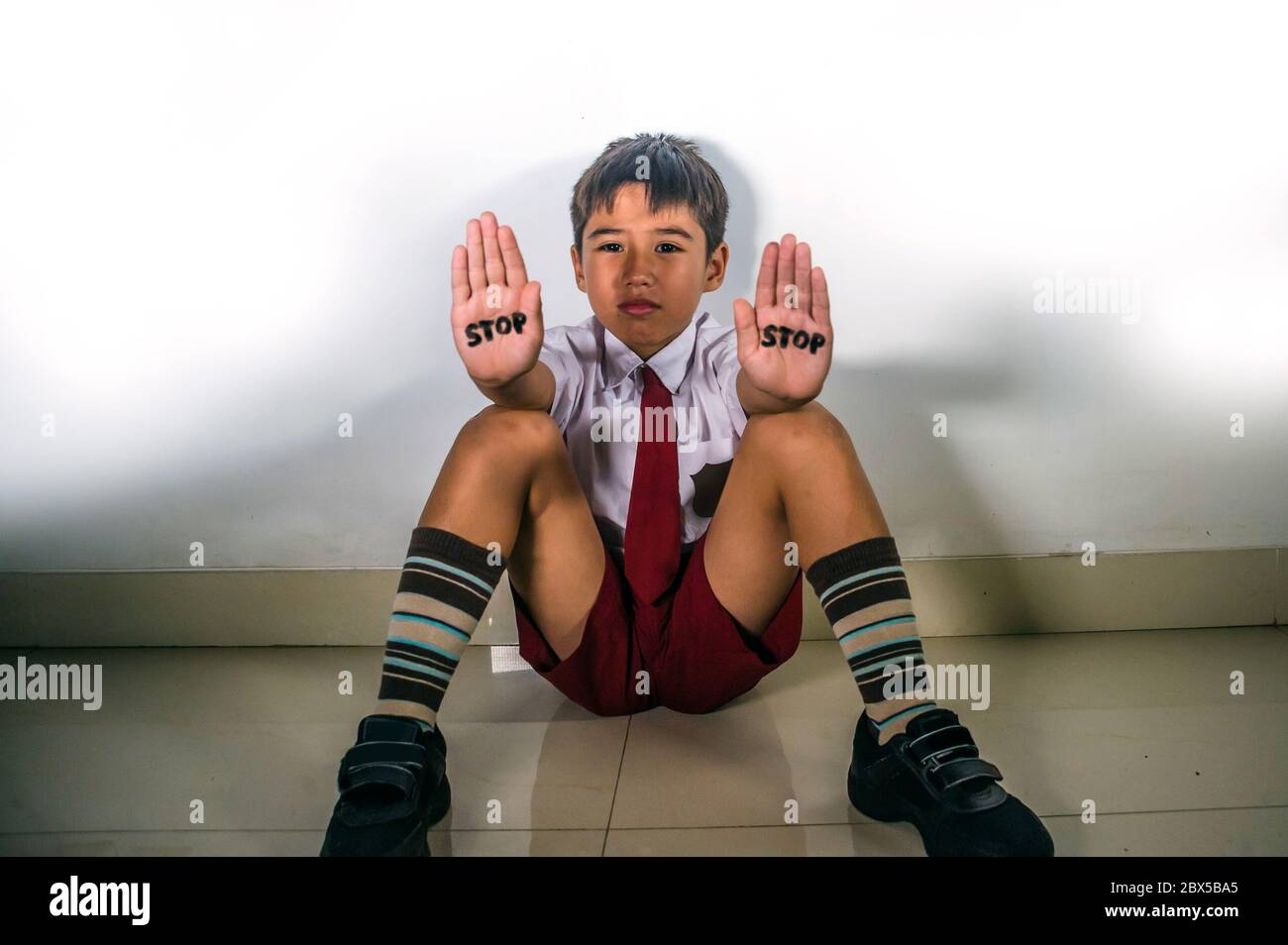 lifestyle dramatic isolated portrait of young kid sad and depressed suffering bullying problem and abuse at school with stop word written on his hands Stock Photo