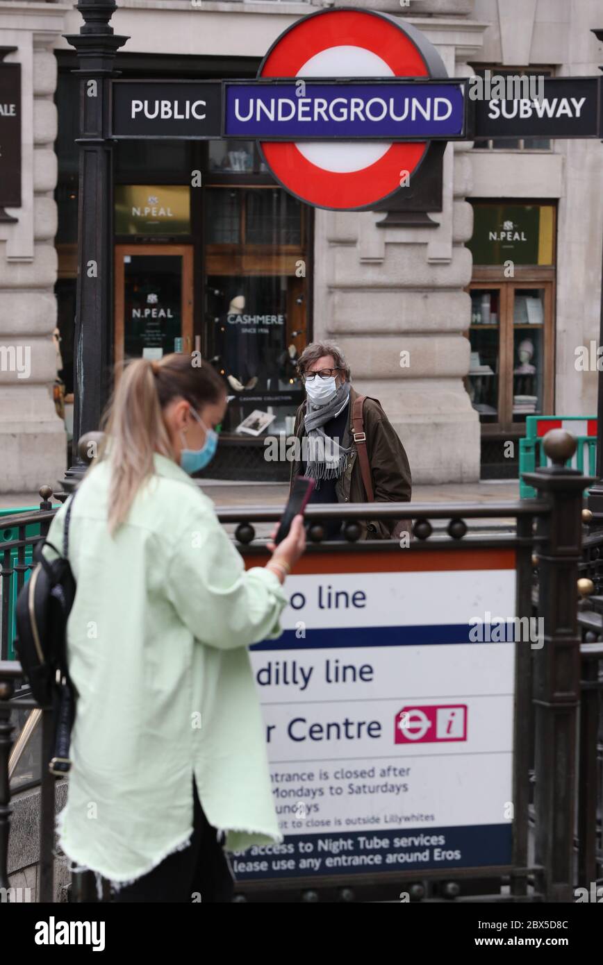 People wearing facemasks pass the entrance to the underground at Piccadilly station, central London, following the announcement that wearing a face covering will be mandatory for passengers on public transport in England from June 15. Stock Photo