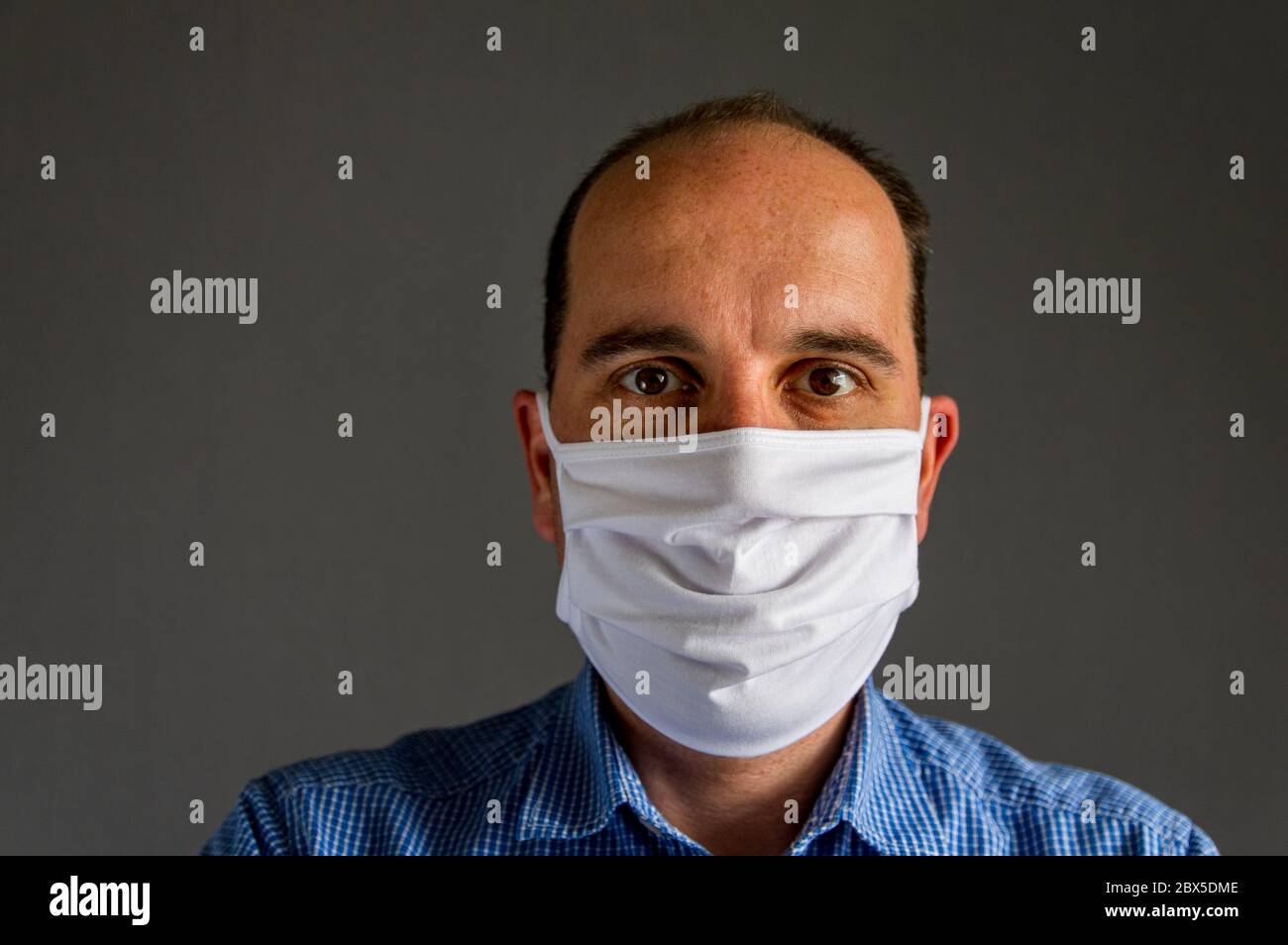 portrait of a young caucasian man wearing a protective face mask in front of a gray background. Studio shot with natural light. Stock Photo