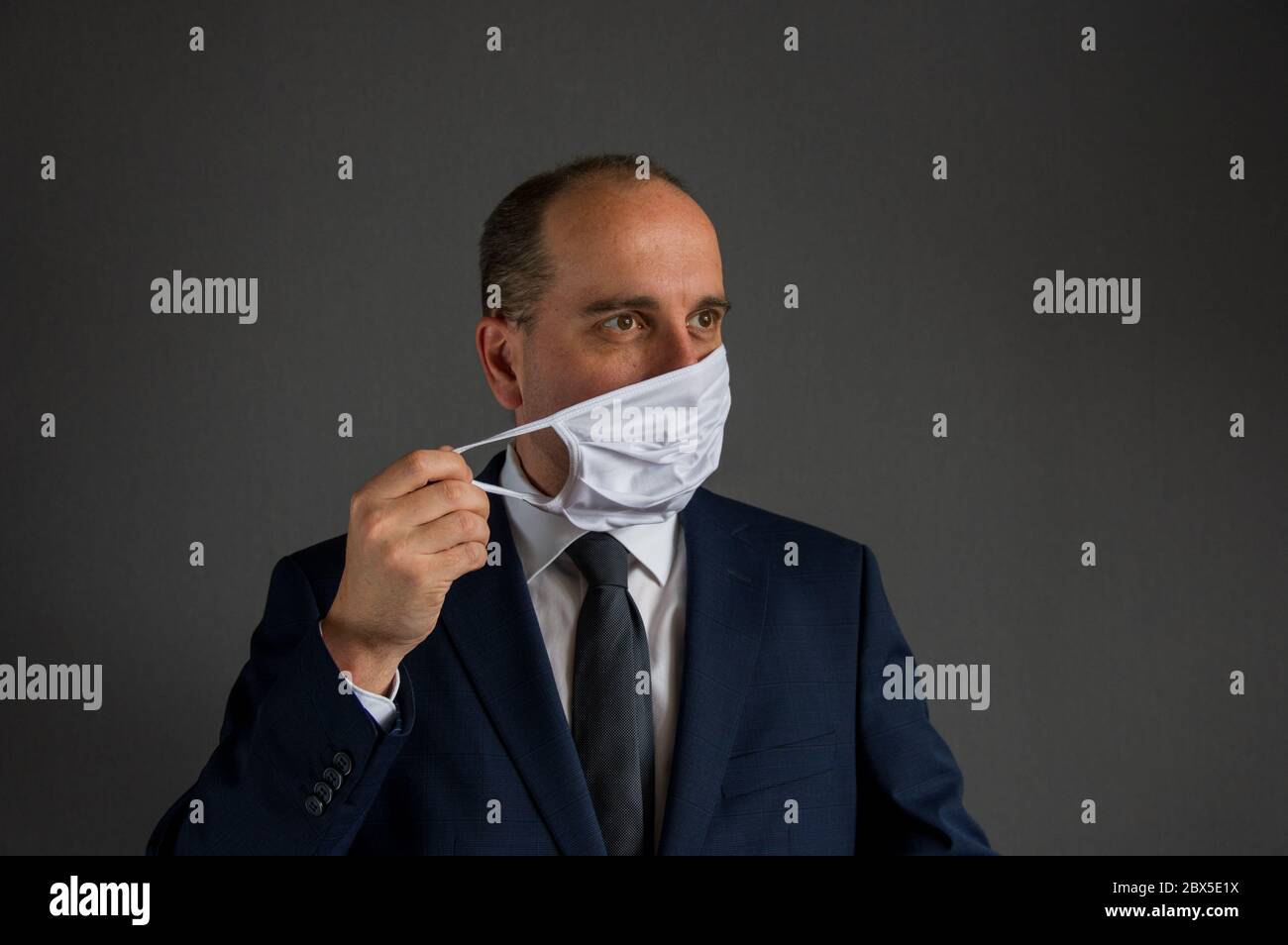 portrait of a smart dressed business man with suit and tie taking off his protective face mask looks into the distance off camera. Concept of hope for Stock Photo