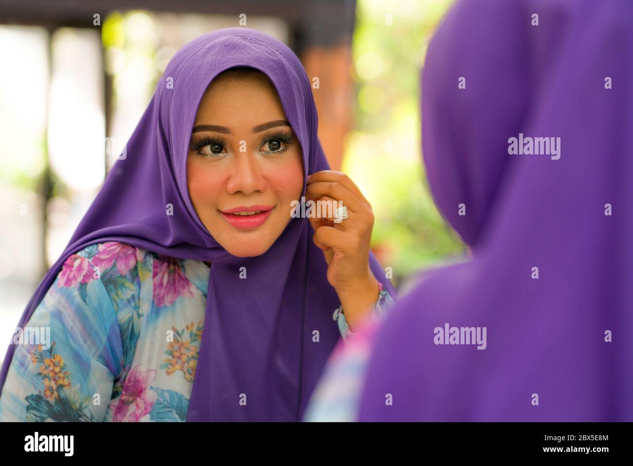 mirror reflection of young happy and beautiful Muslim woman in traditional hijab adjusting her blue head scarf  cheerful dolling up in beauty and fash Stock Photo
