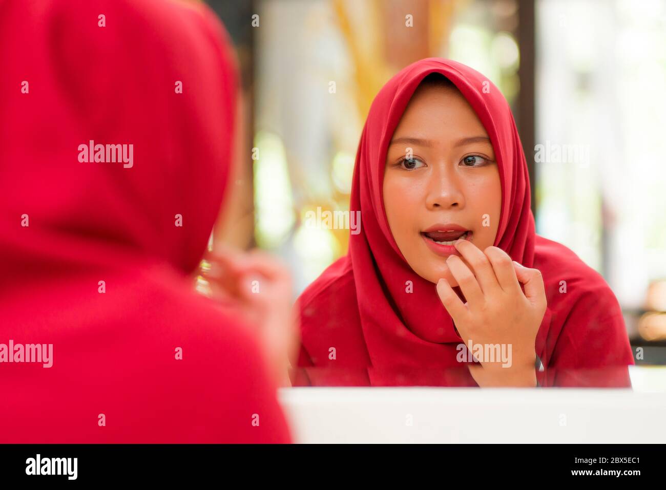 mirror reflection of young happy and beautiful Muslim woman in traditional hijab head scarf applying make up and cosmetics cheerful dolling up in beau Stock Photo