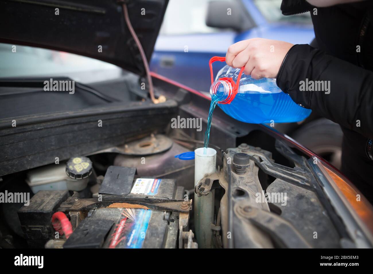 Detail on pouring anti-freeze liquid screen wash into dirty car from blue anti-freeze water container, car concept Stock Photo
