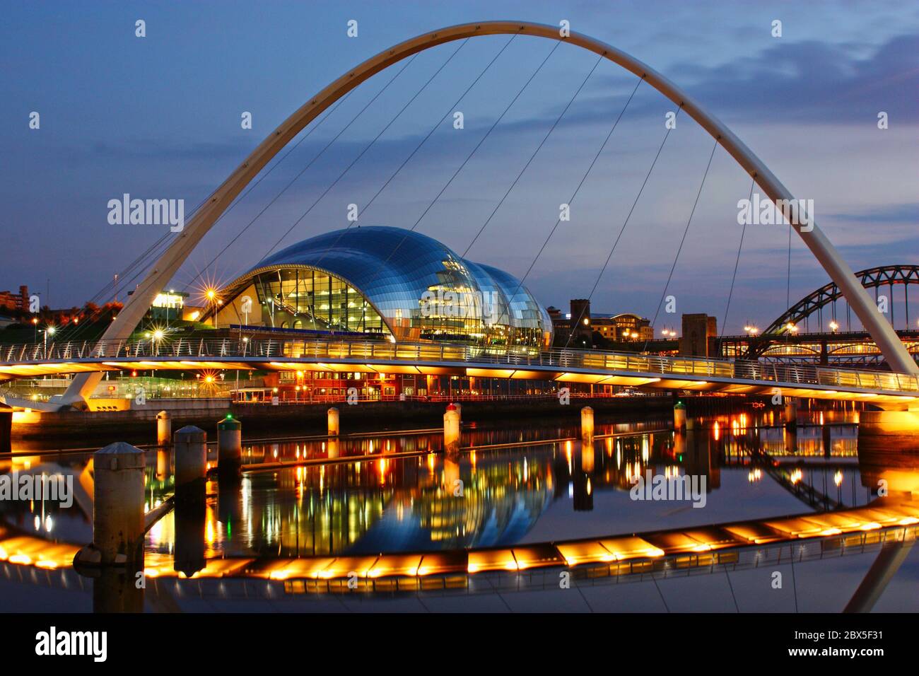 The Gateshead Millennium Bridge, Sage Centre and Newcastle's Tyne Bridge taken at dusk in the blue hour with lights reflected in the still river water Stock Photo