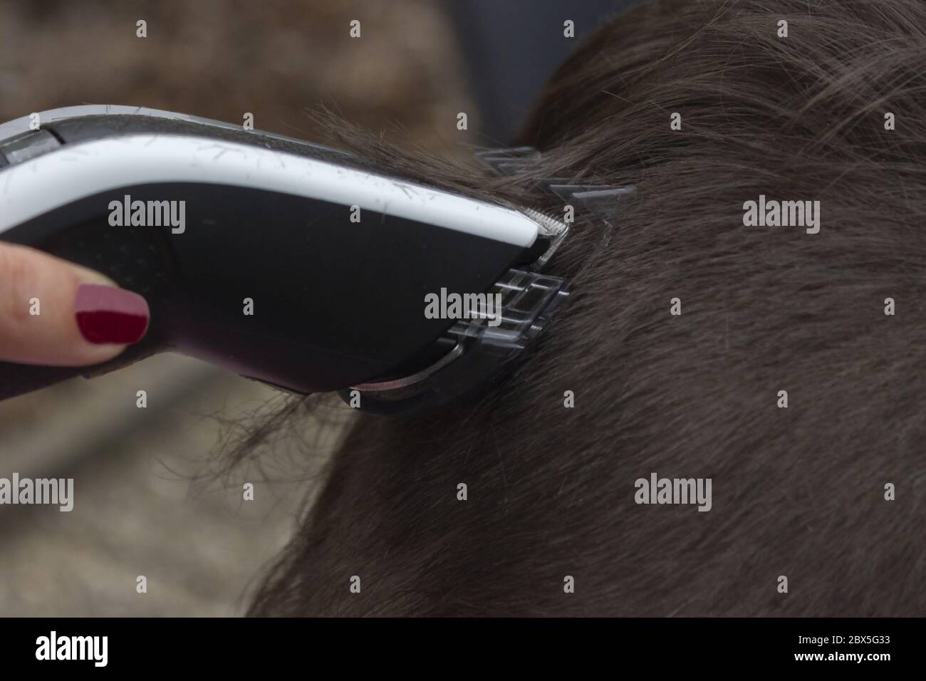 Detail of a haircut by a hairdresser. The hairdresser holds in hand a electric razor. Stock Photo