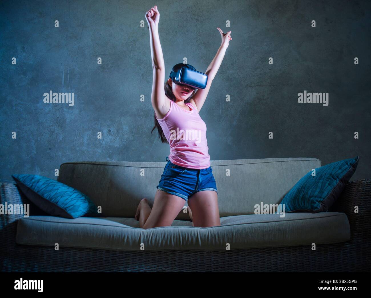 young woman at home sofa couch playing video game using VR virtual reality goggles watching in 3 dimension enjoying curious having fun amazed with the Stock Photo