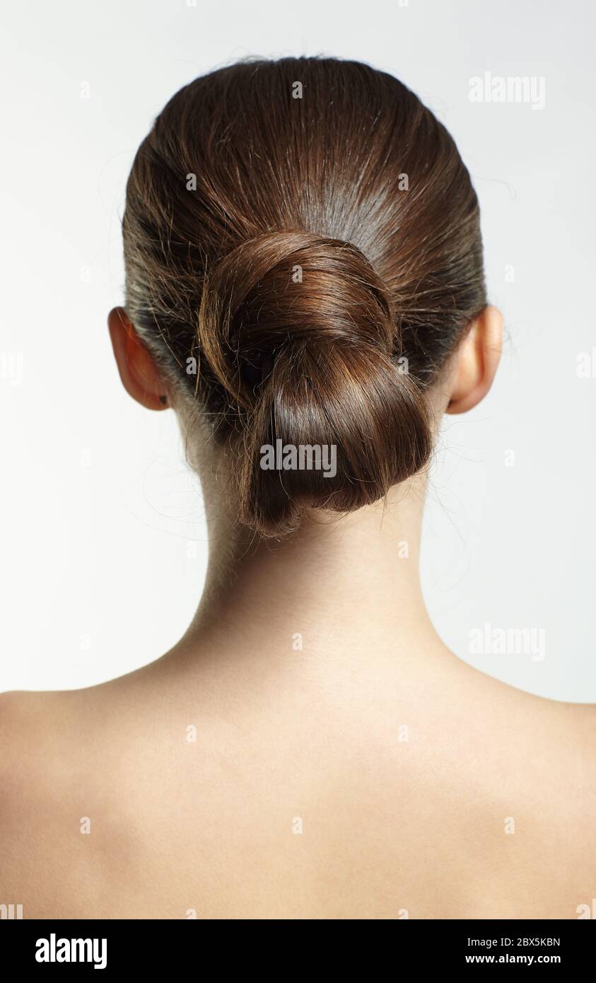 Back view portrait of beautiful young dark brunette woman. Female with creative hairdo on gray background. Stock Photo