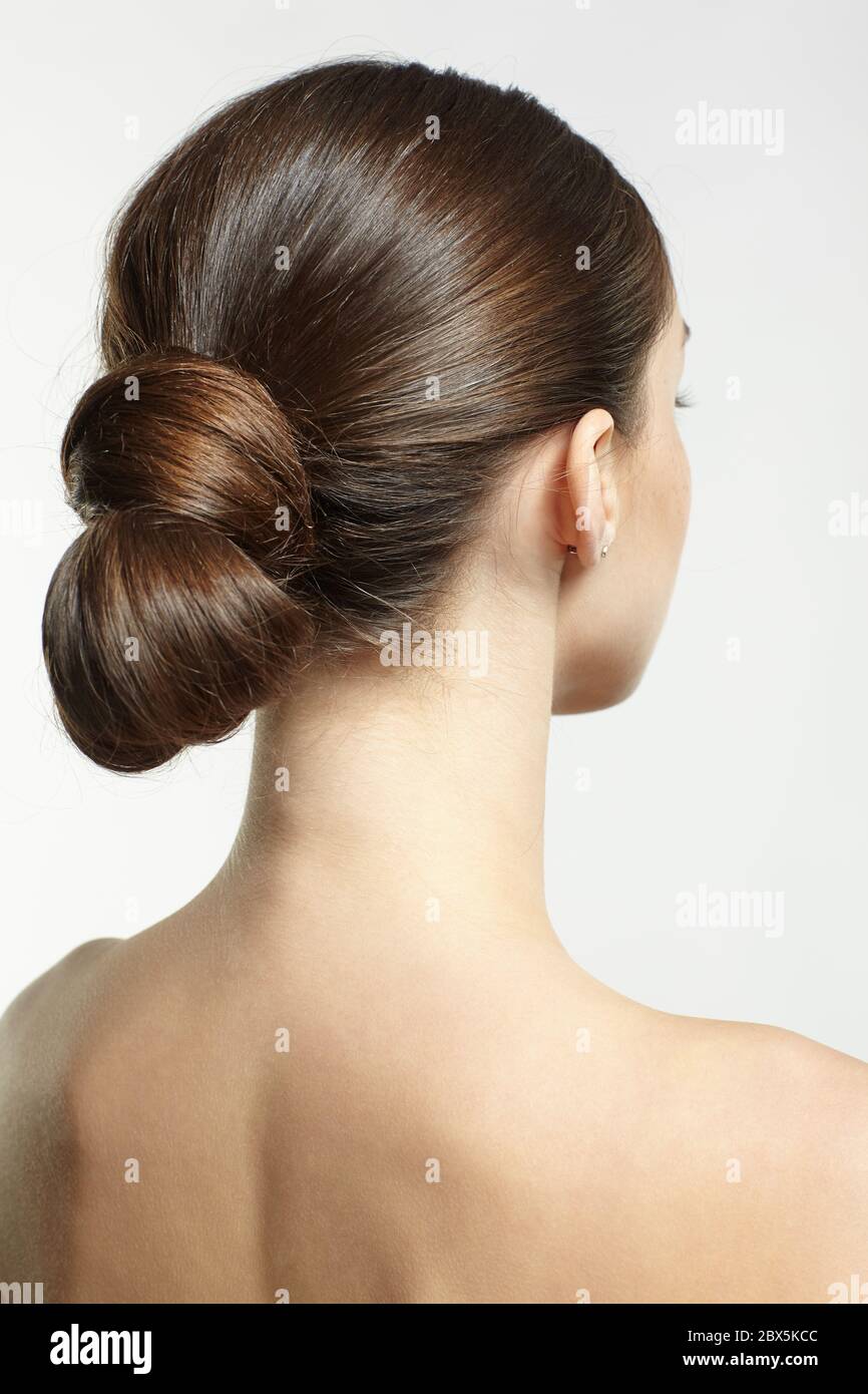 Back view portrait of beautiful young dark brunette woman. Female with creative hairdo on gray background. Stock Photo