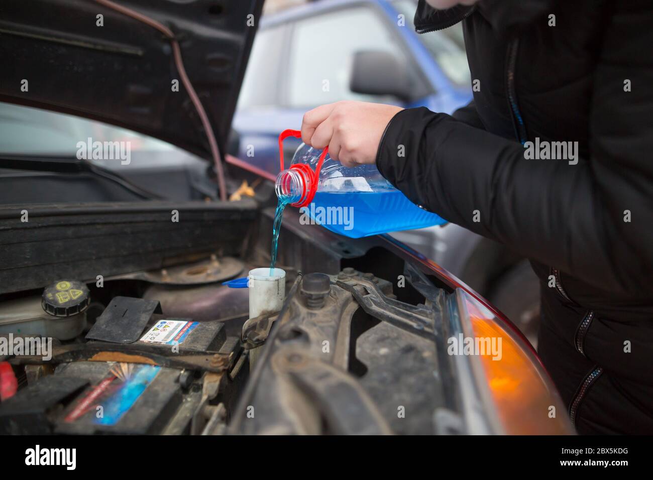 Detail on pouring anti-freeze liquid screen wash into dirty car from blue anti-freeze water container, car concept Stock Photo