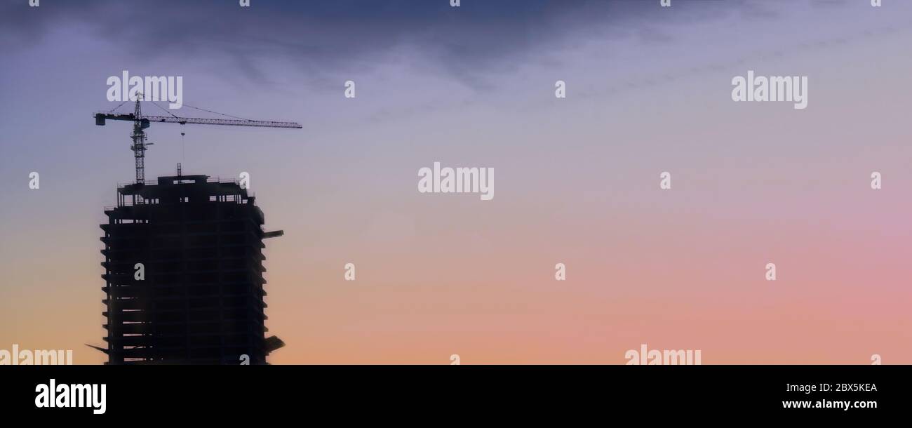 Silhouette of a tall building with tower crane on purple sky background with copy space. Stock Photo