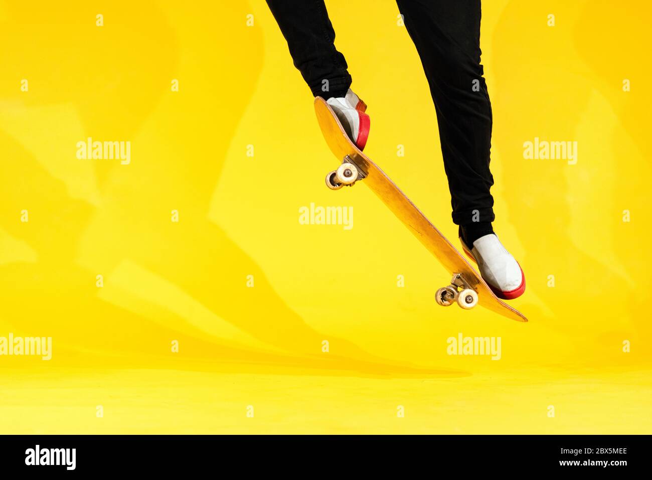 Skateboarder performing skateboard trick - ollie on concrete. Studio shot of olympic athlete practicing jump on yellow background, preparing for compe Stock Photo