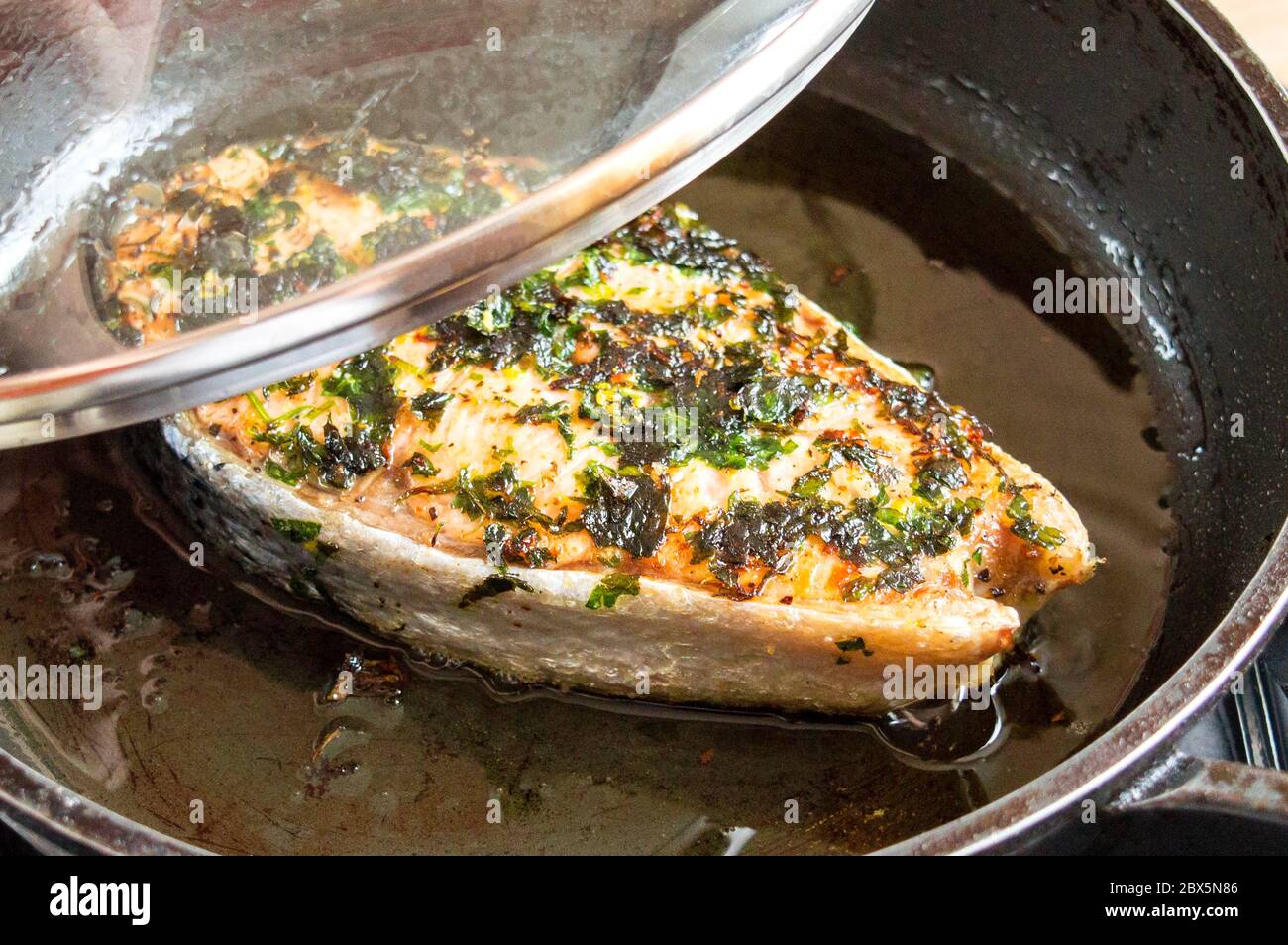 Fried red fish in a pan under the lid. Fry salmon in oil Stock Photo