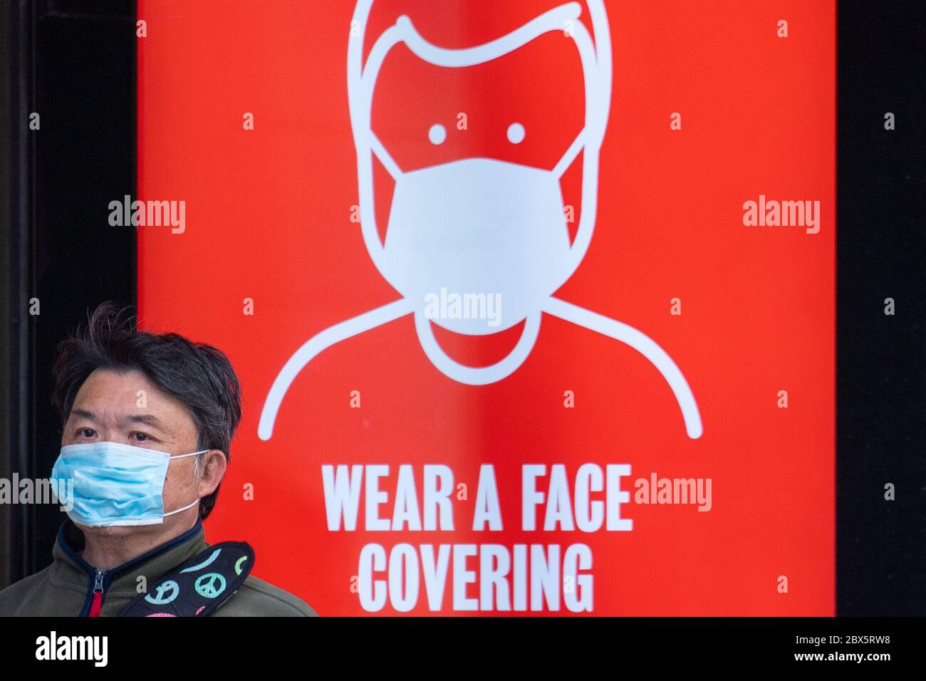 A man wearing a protective face mask waits at a bus stop in central London displaying a notice advising passengers to wear a face covering on public transport, following the announcement that wearing a face covering will be mandatory for passengers on public transport in England from June 15. Stock Photo