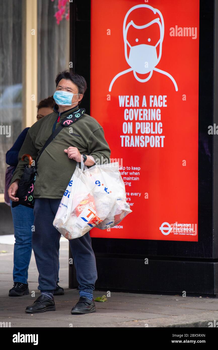 A man wearing a protective face mask waits at a bus stop in central London displaying a notice advising passengers to wear a face covering on public transport, following the announcement that wearing a face covering will be mandatory for passengers on public transport in England from June 15. Stock Photo
