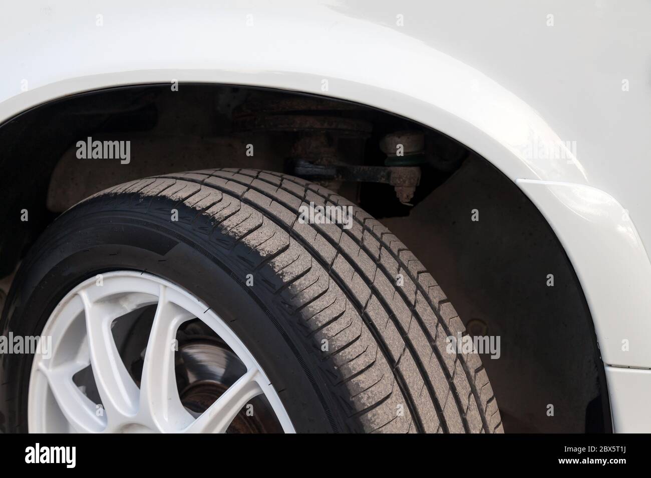 Summer black tire under the wing of a white Russian car VAZ 2114 close-up with a disk. Seasonal wheel replacement in a car workshop. Stock Photo