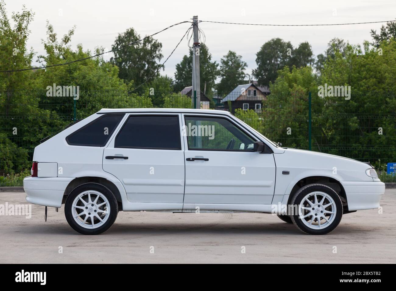 Novosibirsk, Russia - 05.20.2020: White Russian car sedan brand LADA model 2114 side with wheels and a summer tire on a background of green trees and Stock Photo