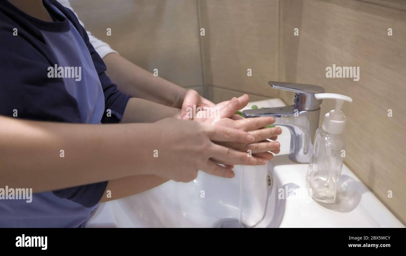 Mother and boy washing their hands together. Mom helps her son wash soap suds from his hands under running water. Parenthood concept Stock Photo