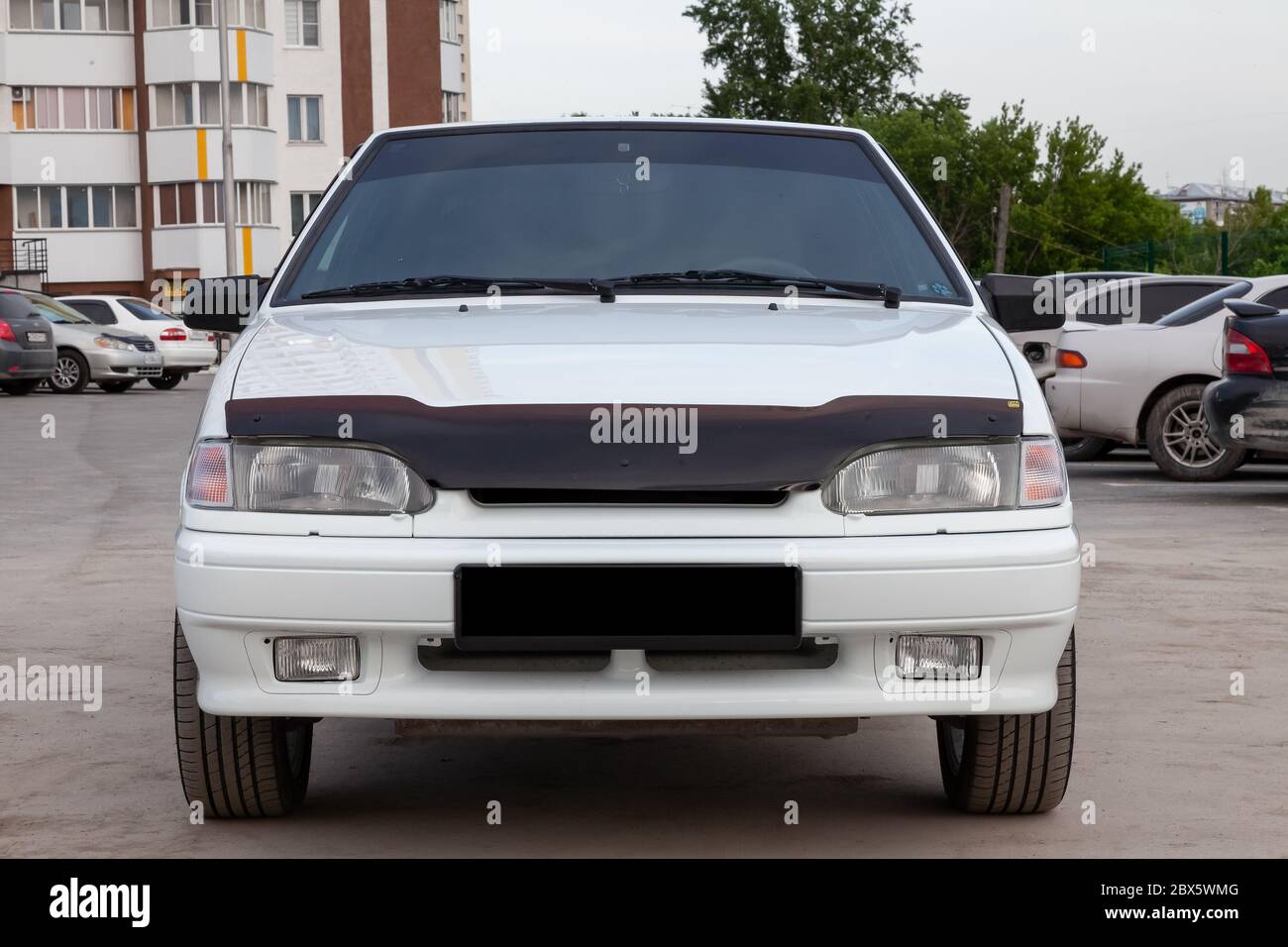 Novosibirsk, Russia - 05/20/2020: front part of a white Russian car brand VAZ model 2114 on the background of an apartment building and cars with dire Stock Photo