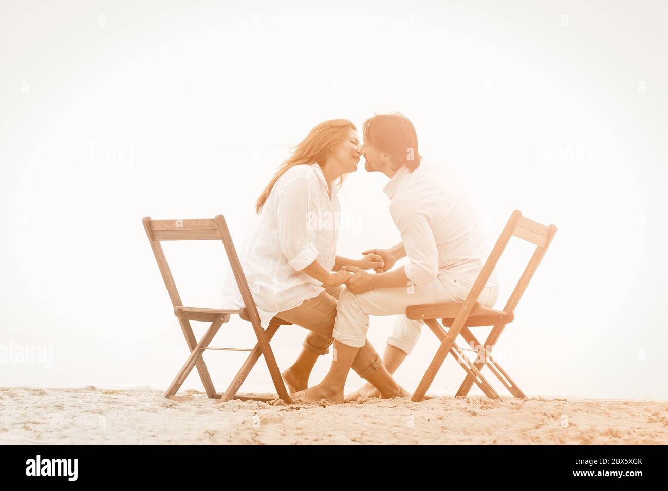 View of Lovely couple in white clothes kisses holding hands while sitting on ...