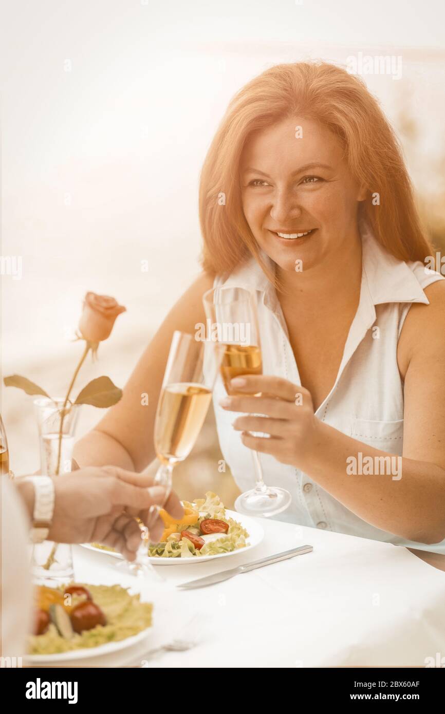 Happy woman drinks white wine with her beloved man. Mature couple clinking wineglasses while sitting in a summer cafe outdoors. Happy together concept Stock Photo