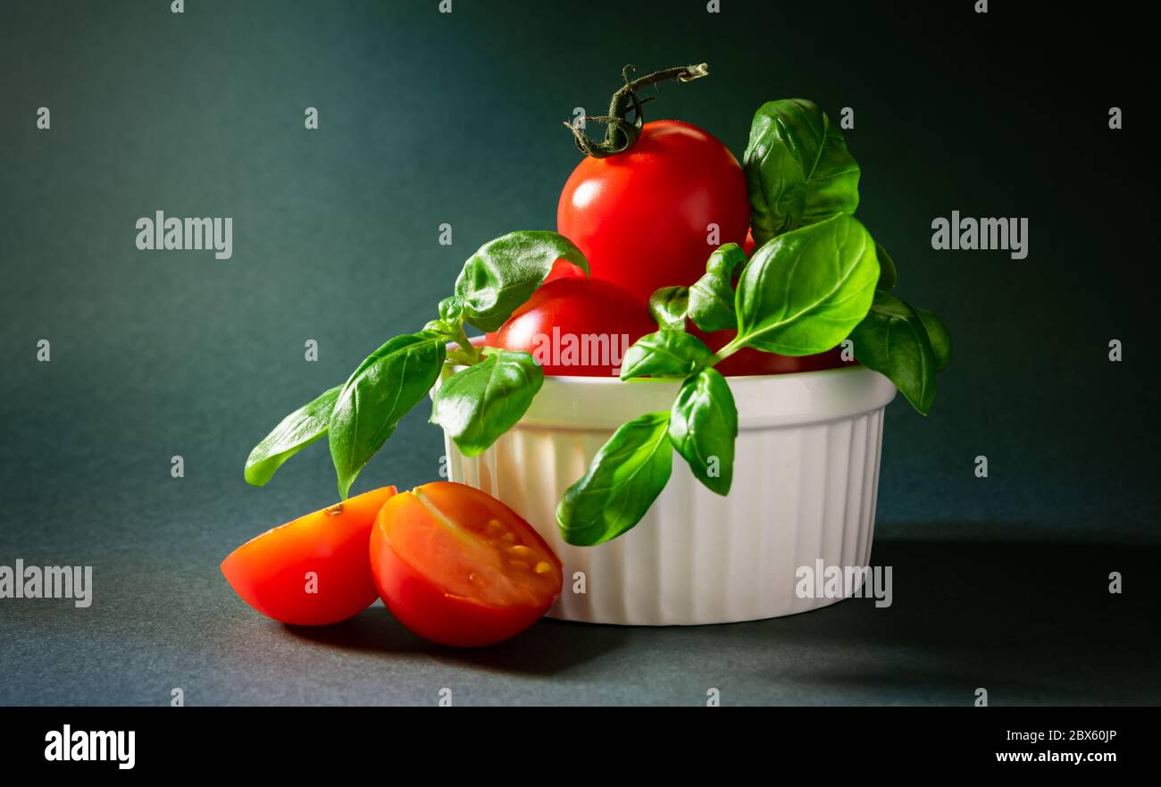 still life, cherry tomatoes with basil leaves in a white plate on a ...