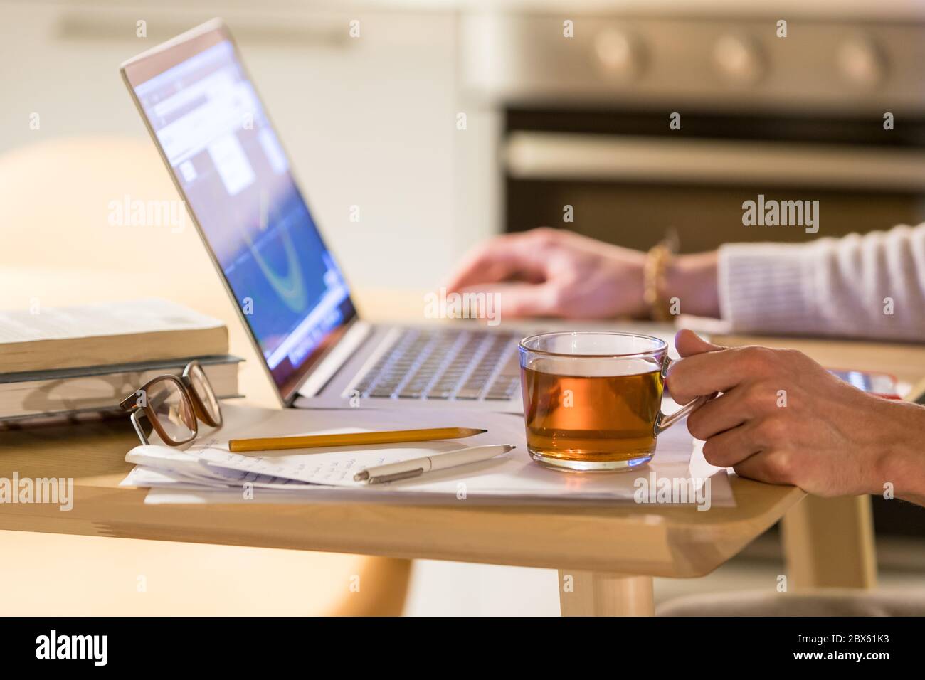 Man freelancer working at home office on laptop, holding on cup of tea