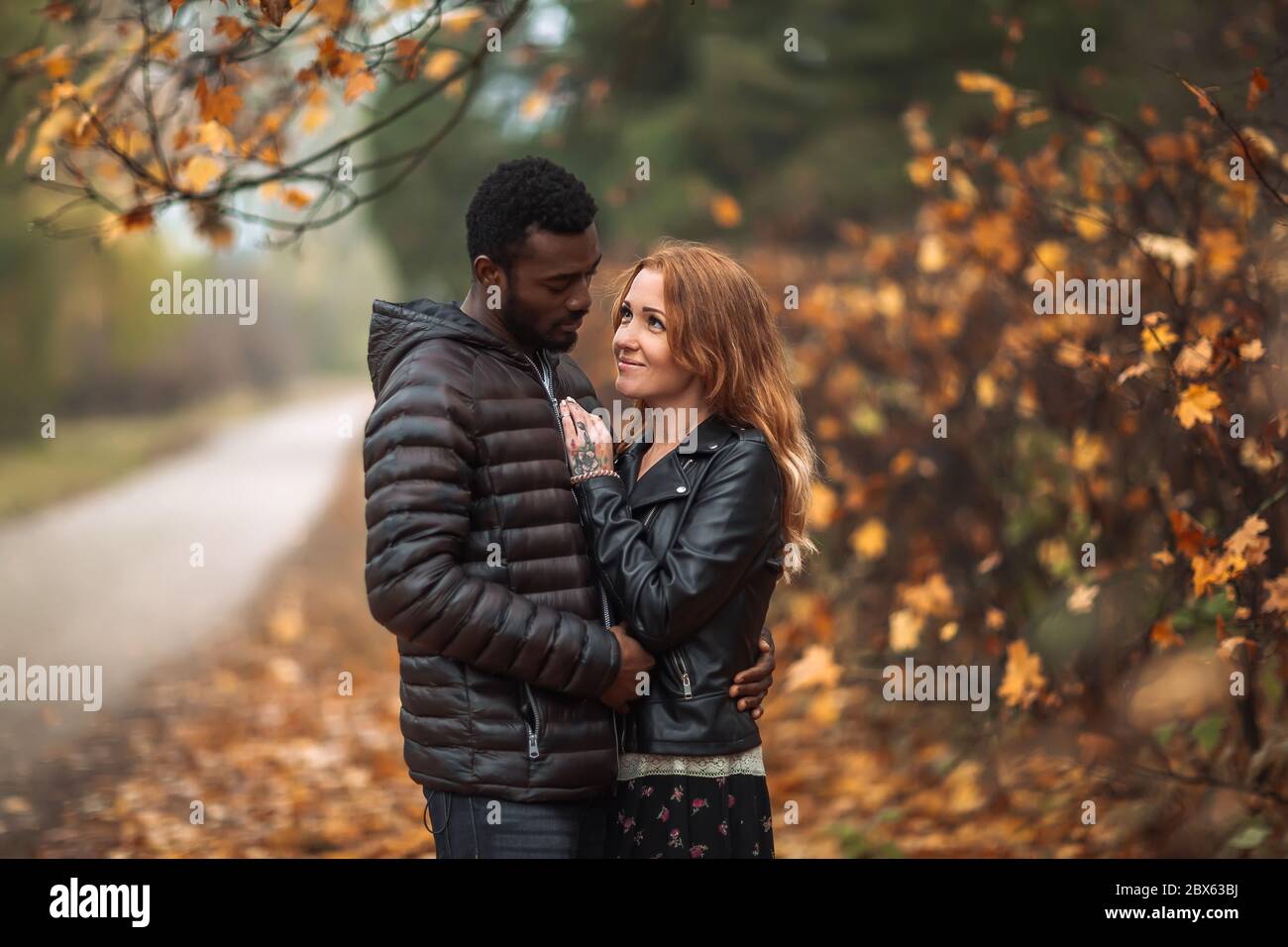 Happy cute Interracial couple posing in blurry autumn park background, black man and white redhead woman Stock Photo