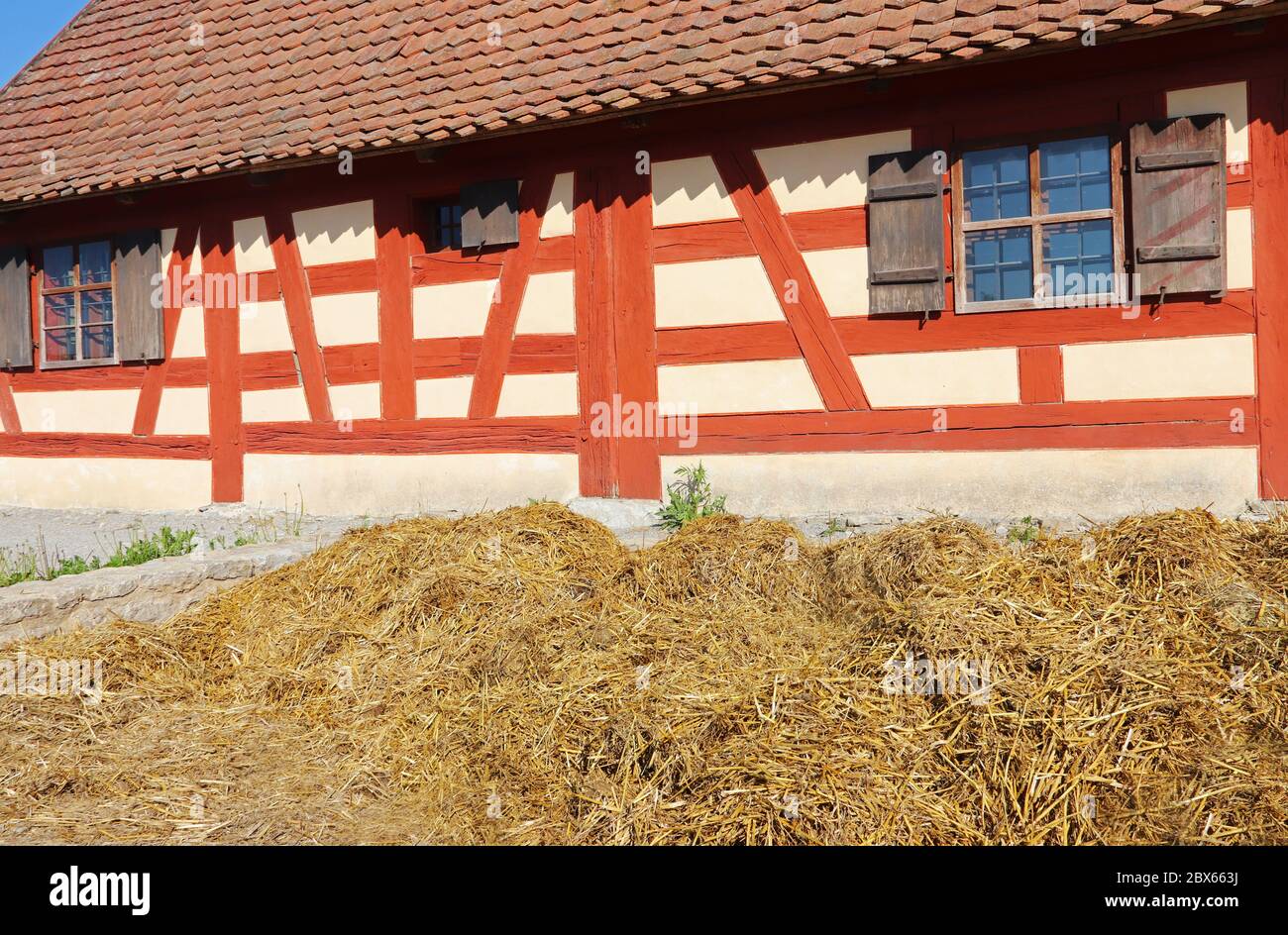 dung heap in front of an old timbered farmhouse with red painted beams, shutters and a dung heap in front of it Stock Photo