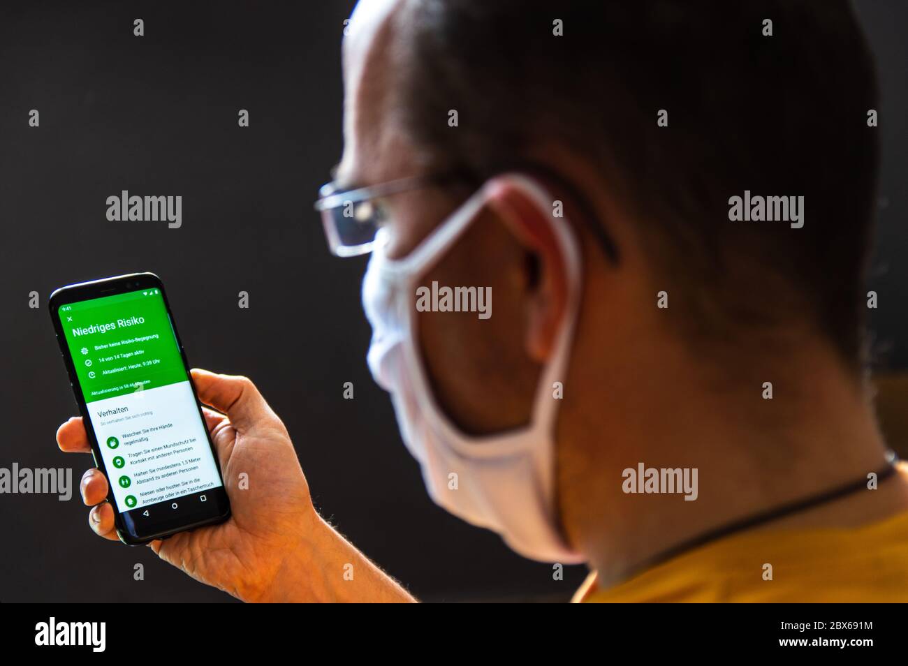 Young man wearing a protective face mask checks the German corona warn app for his infection risk analysis. Niedriges Risiko = German for Low Risk, Stock Photo