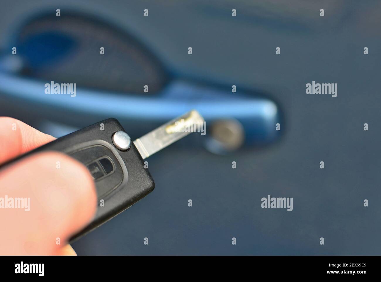 Closeup of hand holding a remote key unlocking the blue car. Stock Photo