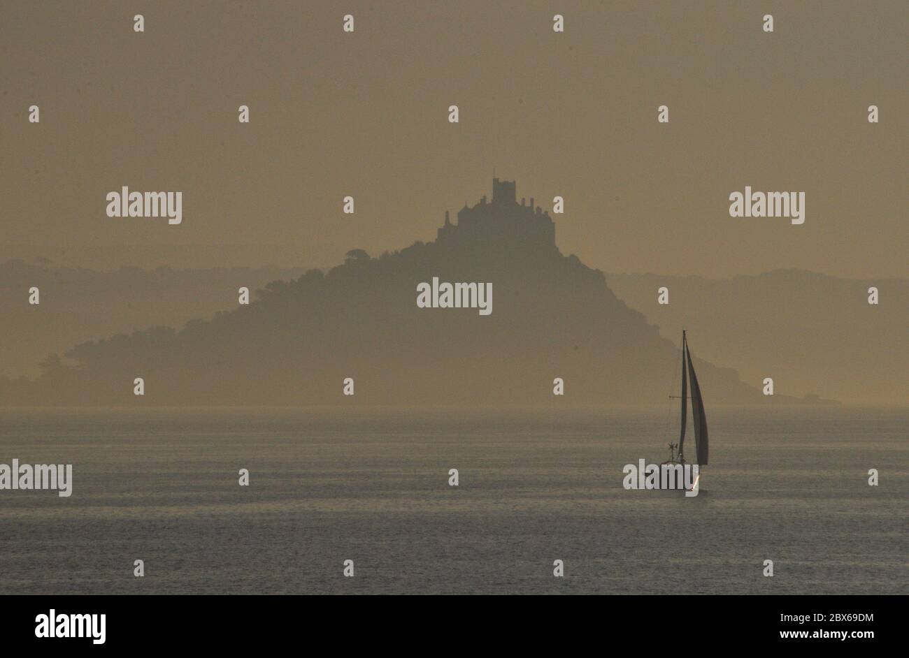 Misty atmospheric view of St Michaels Mount with an early start for a sailing yacht,Mounts Bay, Penzance, Cornwall, UK Stock Photo