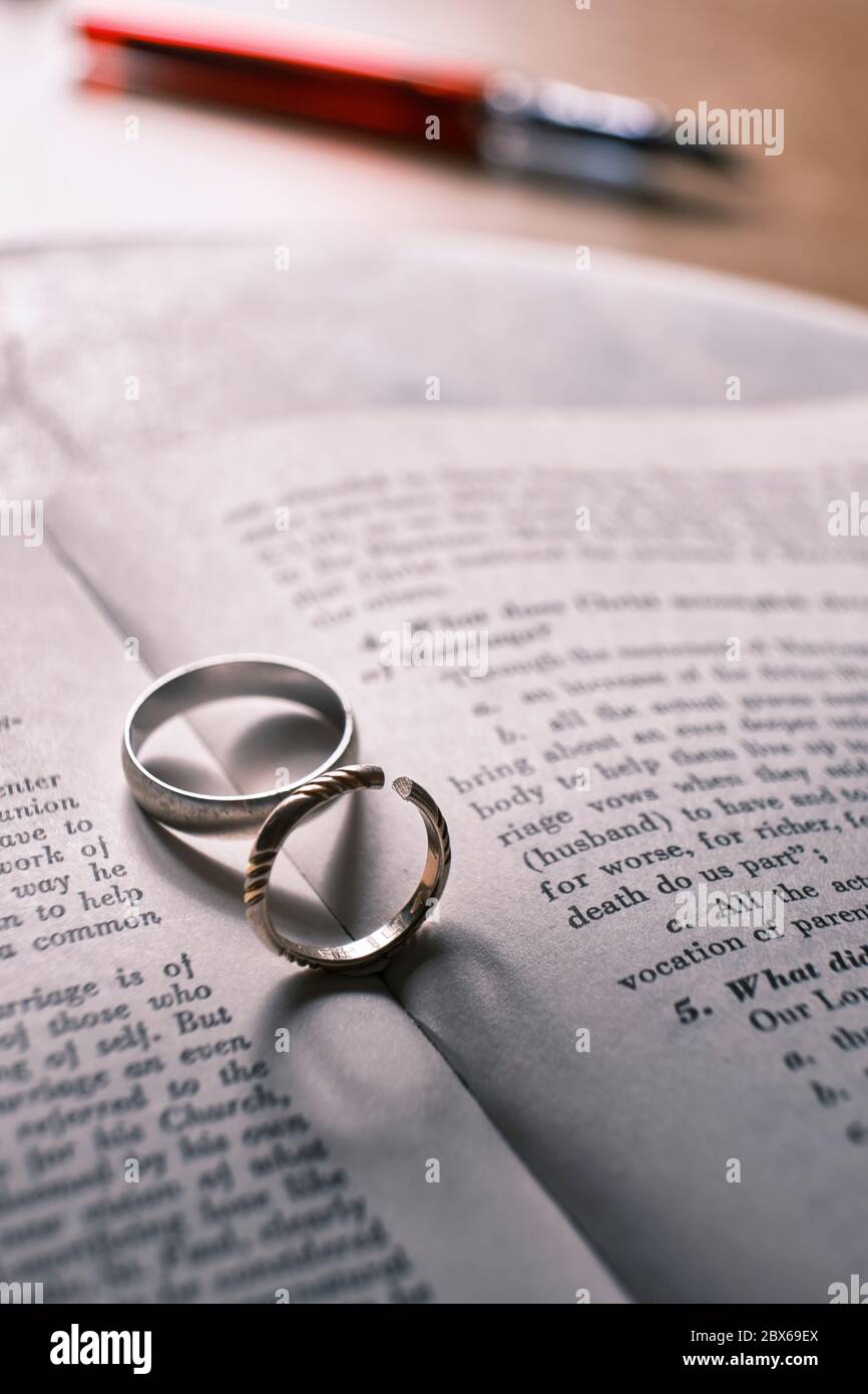 Two wedding bands, one has been cut off on a book with text about marriage. The shadows from the rings make the shape of a heart, and a broken heart. Stock Photo