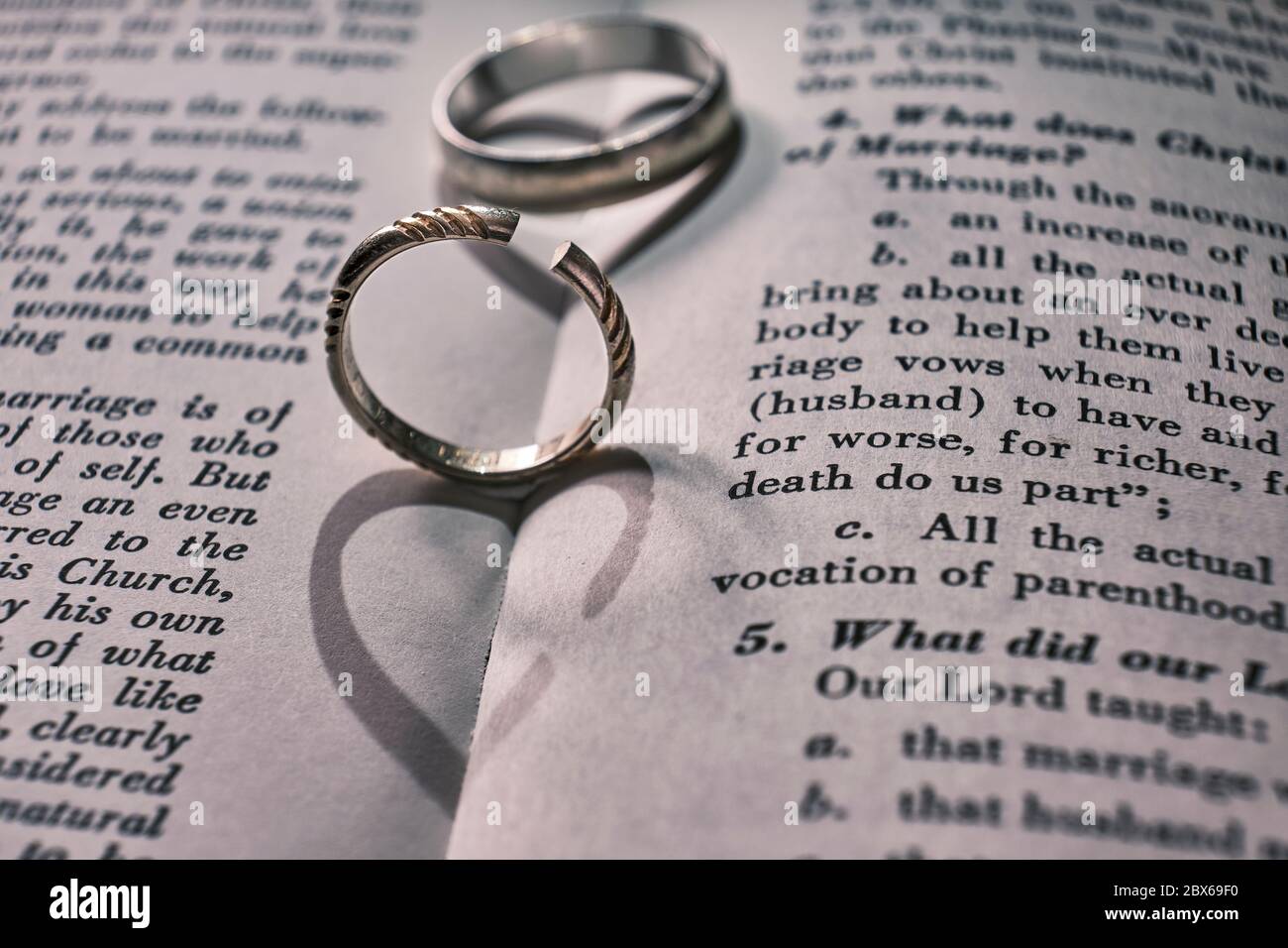 Two wedding bands, one has been cut off on a book with text about marriage. The shadows from the rings make the shape of a heart, and a broken heart. Stock Photo