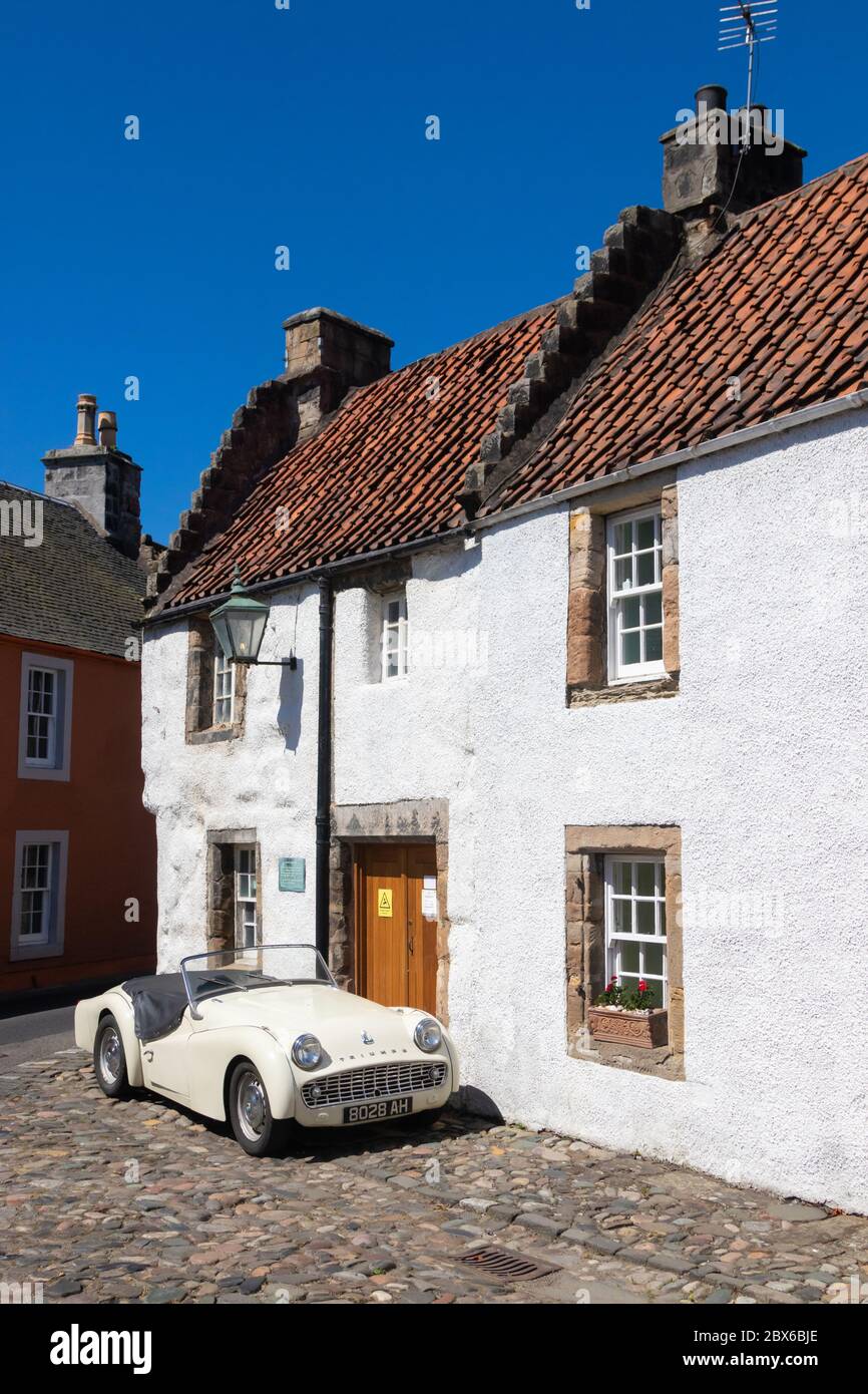 A 1959 Triumph TR3A sports car outside a traditional old house in the