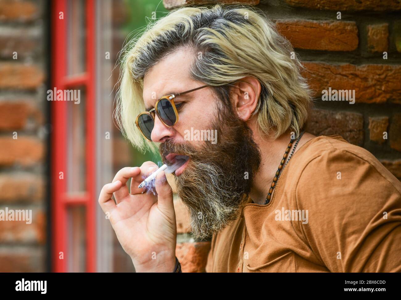 Bearded guy casual style. bad habit concept. harmful for your health. smoke  nicotine addicted. he is heavy smoker. bearded man in glasses relax with  cigarette. brutal mature hipster smoking cigarette Stock Photo -