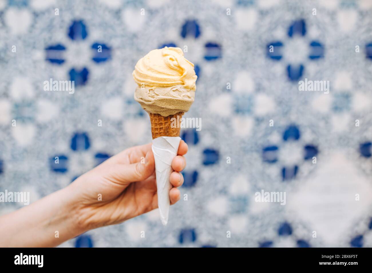 Female hand holding ice cream cone on blurred white blue background Stock Photo