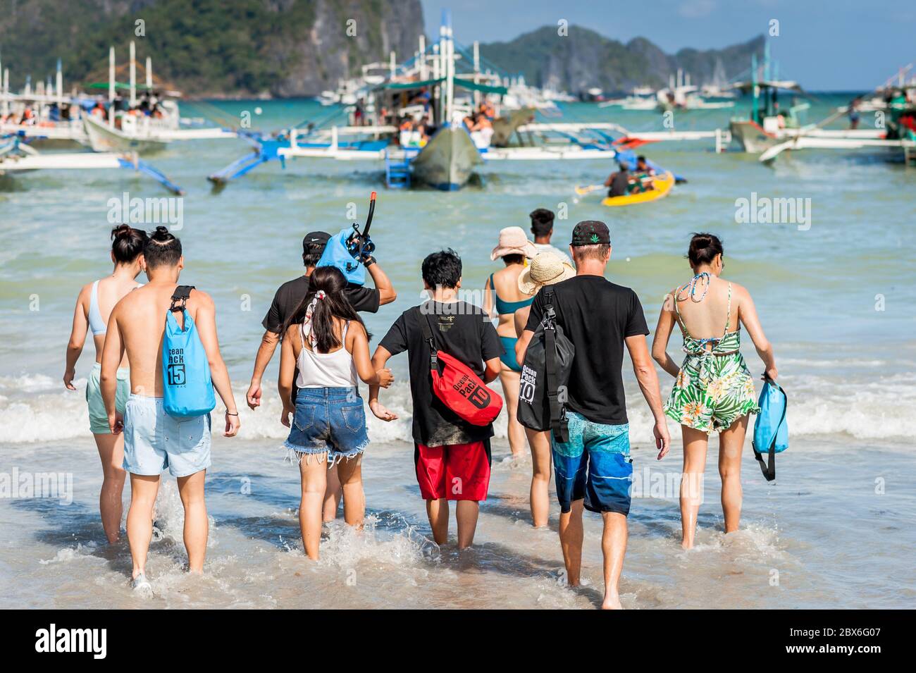 Tourists at El Nido Town beach wade out to the numerous long tail