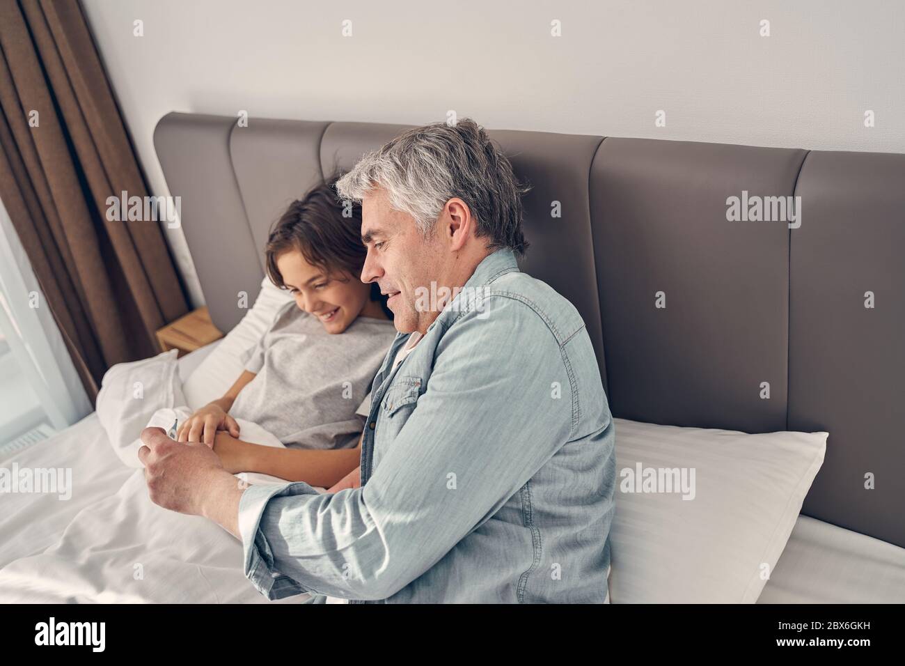 Child staying in bed with his dad next to him Stock Photo Alamy