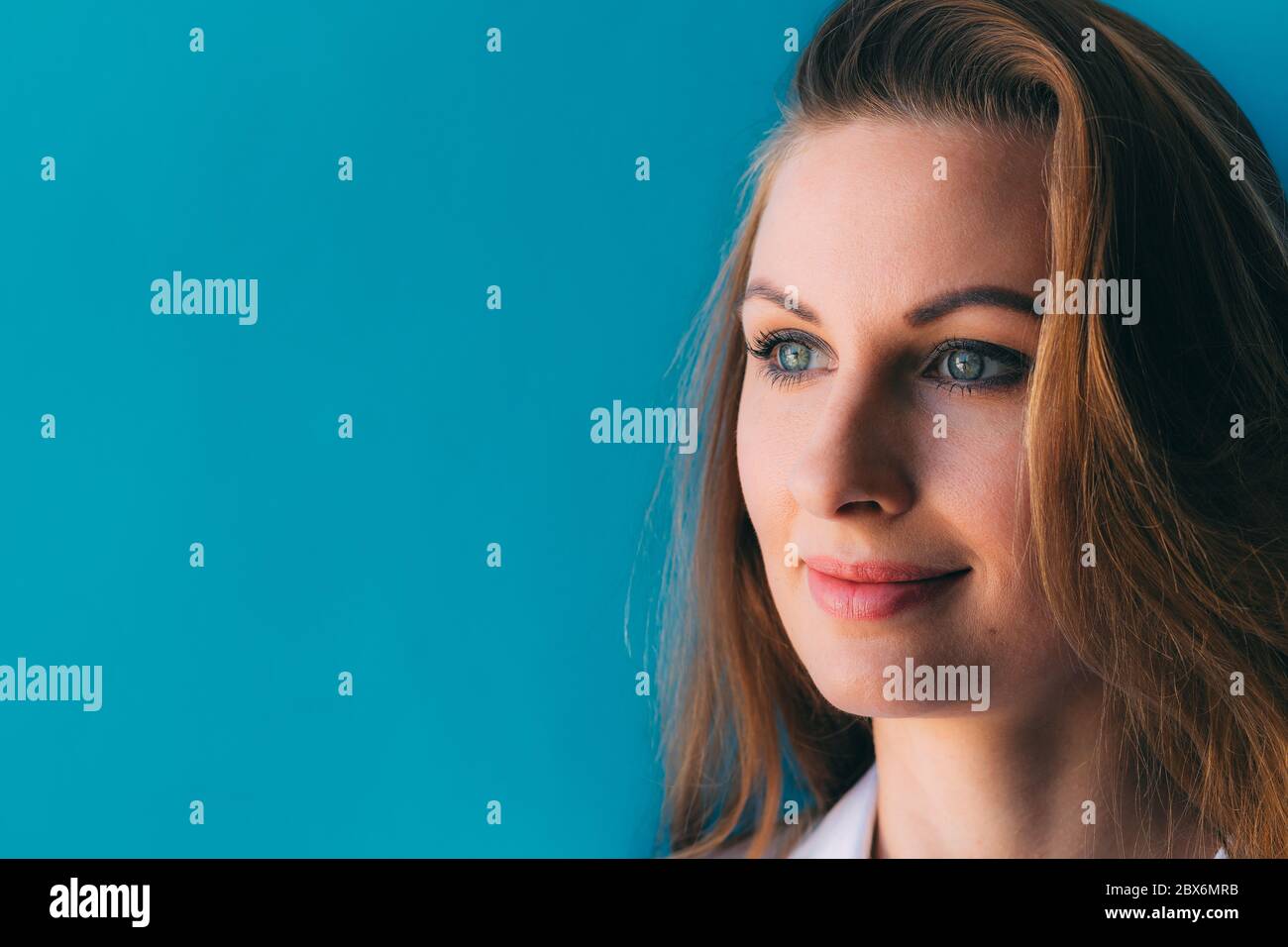Close-up portrait of beautiful young happy woman on blue background, with space for slogan or text. Nice makeup on face. Beauty. Skin care concept. Am Stock Photo