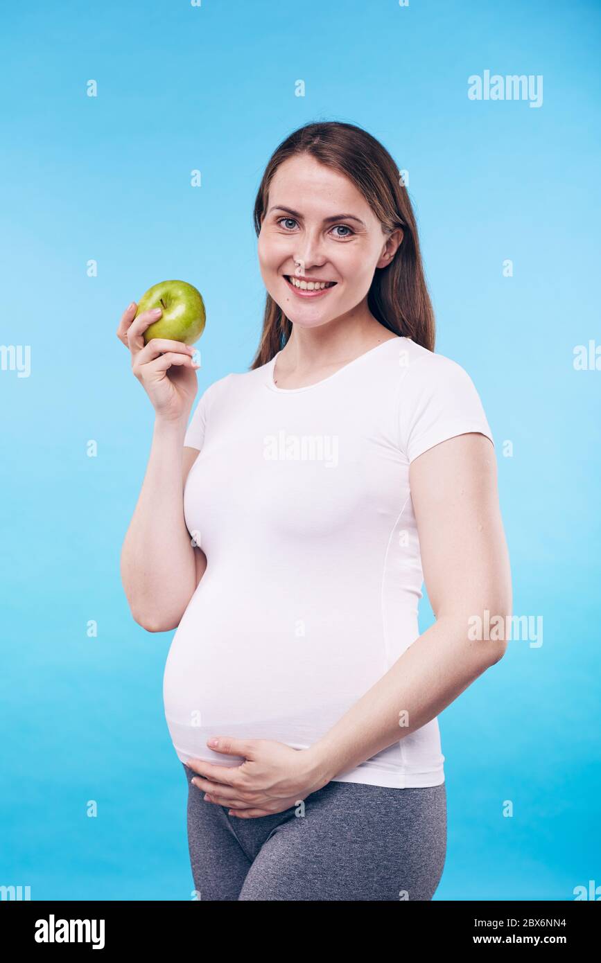 Happy pregnant female with granny smith apple touching bottom of her