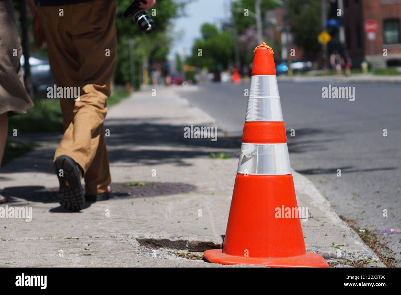 Close up of a safety cone marking a pothole in the pavement as a couple walk by in the summer