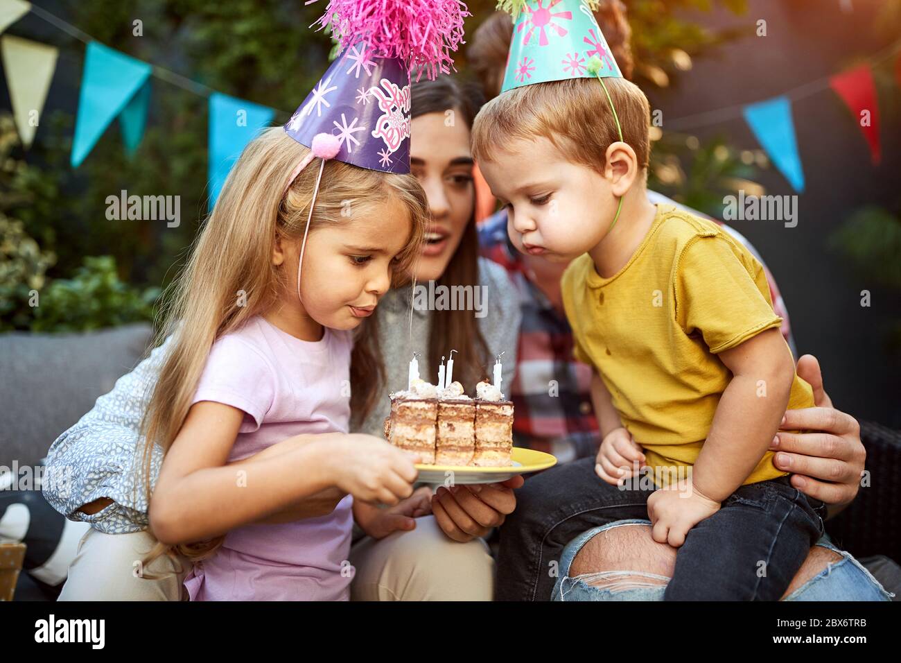 happy Kids with birthday hats blowing candles on the cake Stock Photo