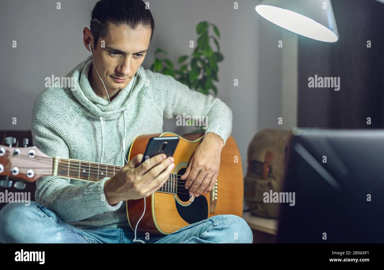 A young musician is learning to play acoustic guitar in an online lesson  using a phone