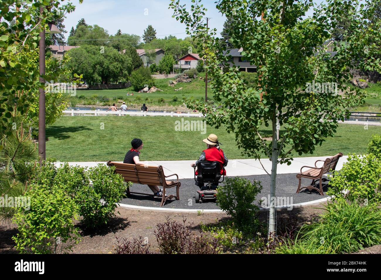 Younger woman and older disabled woman having a socially distant conversation at a public park. Stock Photo