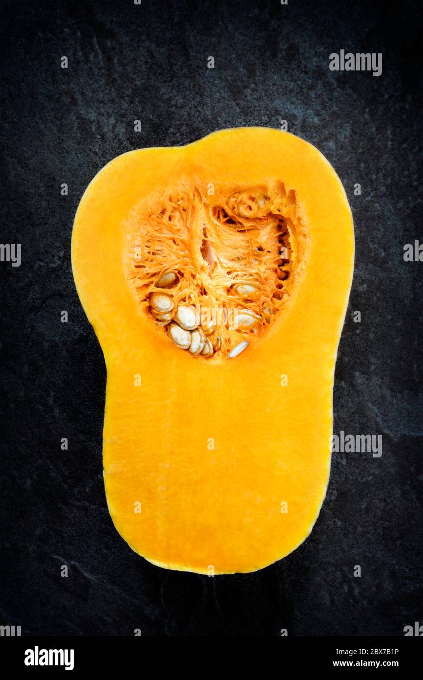 Butternut pumpkin or squash, cut in half, top view over dark stone background. Stock Photo