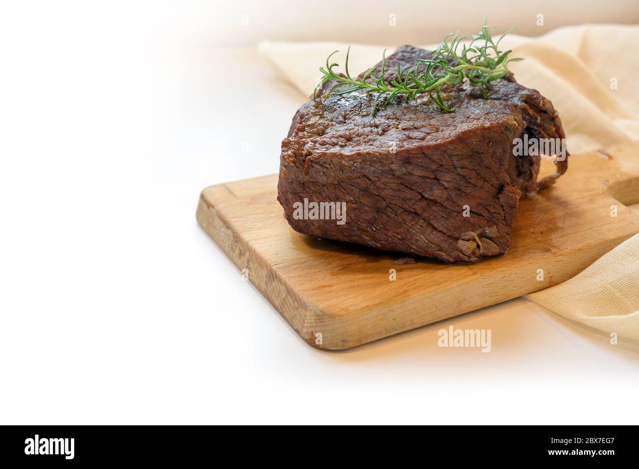 Piece of roast beef braised in red wine with thyme garnish on a cutting board, typical preparation for boeuf bourguignon, the light background is fadi Stock Photo