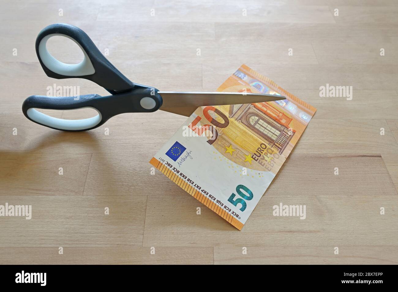 Business concept, fifty Euro banknote is cut with scissors, symbol for wage reduction or pay less money, wooden table, copy space, selected focus Stock Photo