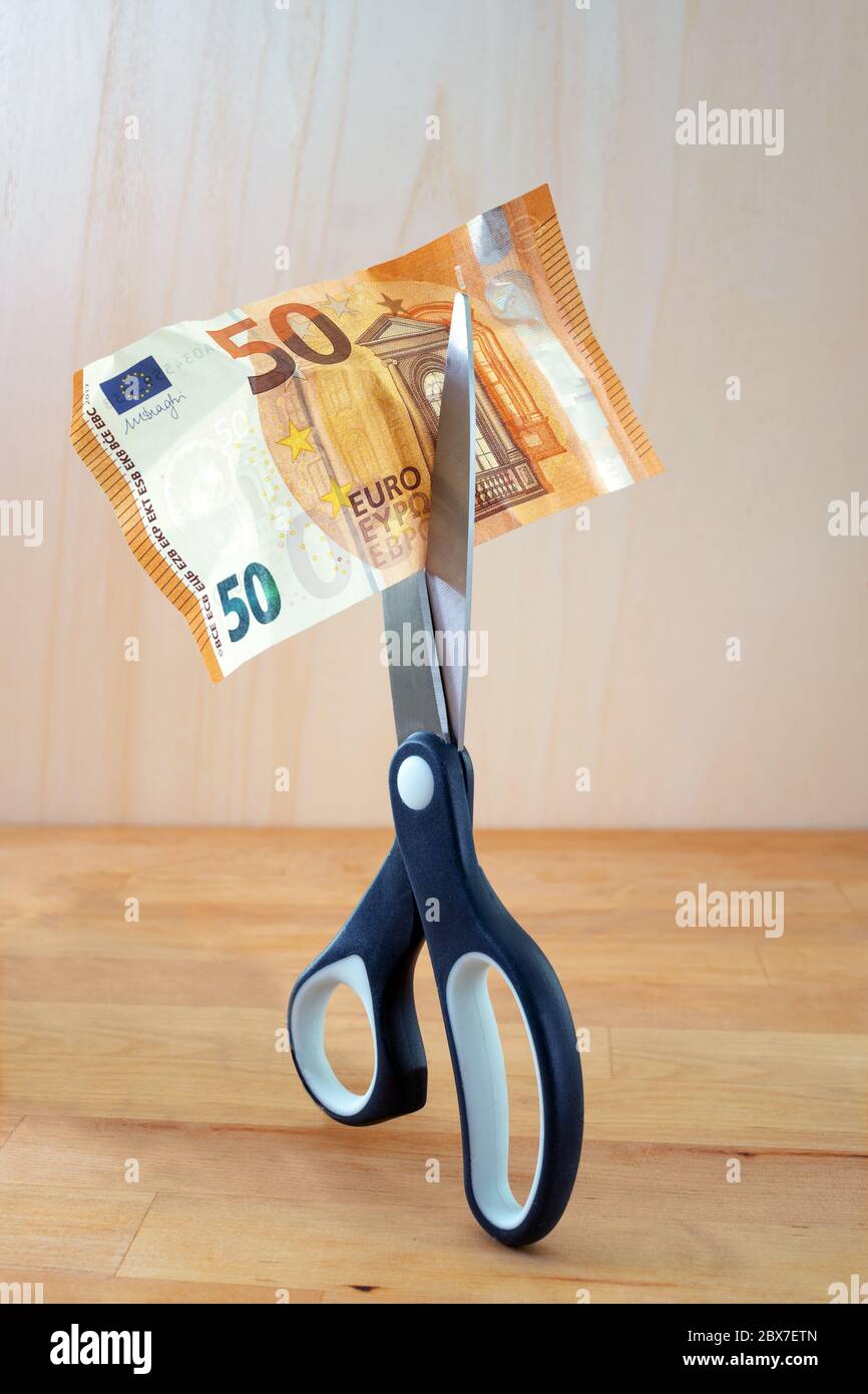 Euro banknote is cut with scissors, business concept or metaphor for income reduction during a financial crisis like coronavirus pandemic, wooden back Stock Photo