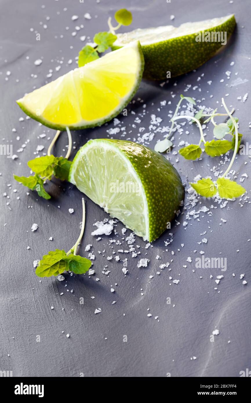 Lime wedges with sea salt and micro herbs, over dark slate. Stock Photo