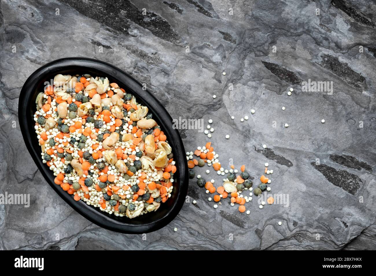 Dried lentils, quinoa and beans in black rustic bowl over slate. Top